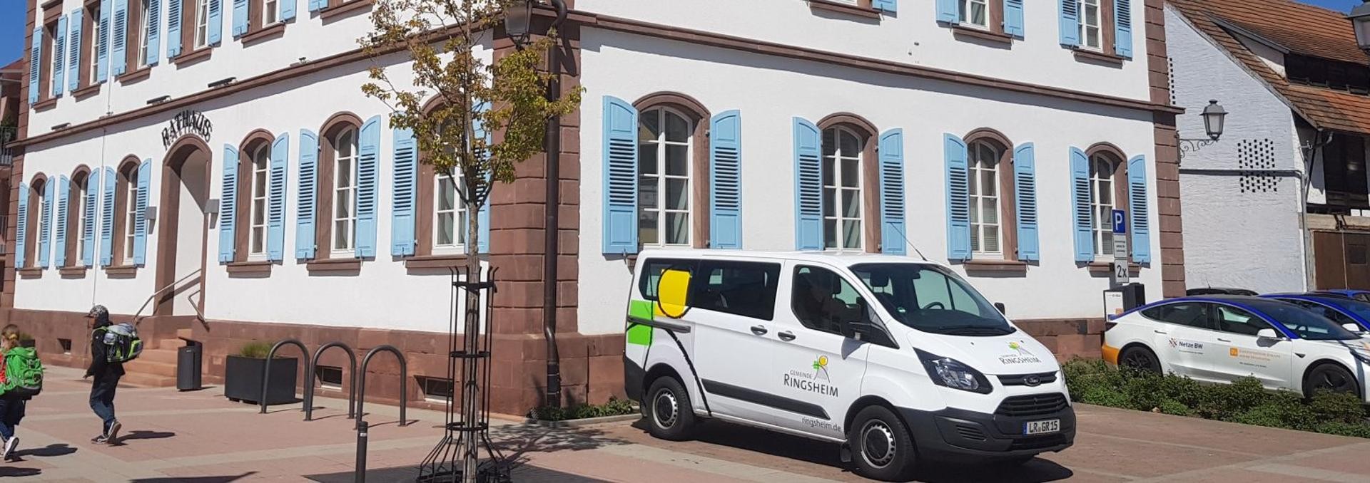 Rathaus mit Gemeindemobil und Stromladesäule Rathaus mit Gemeindemobil und Stromladesäule